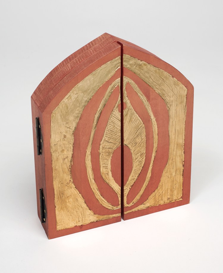 Photo of closed altar piece standing on table - hinges visible at left edge - double doors with gold leaf and carving detail of a vulva