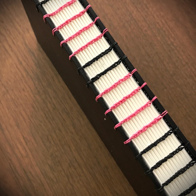 Photo of spine on coptic-bound book with pink and black thread