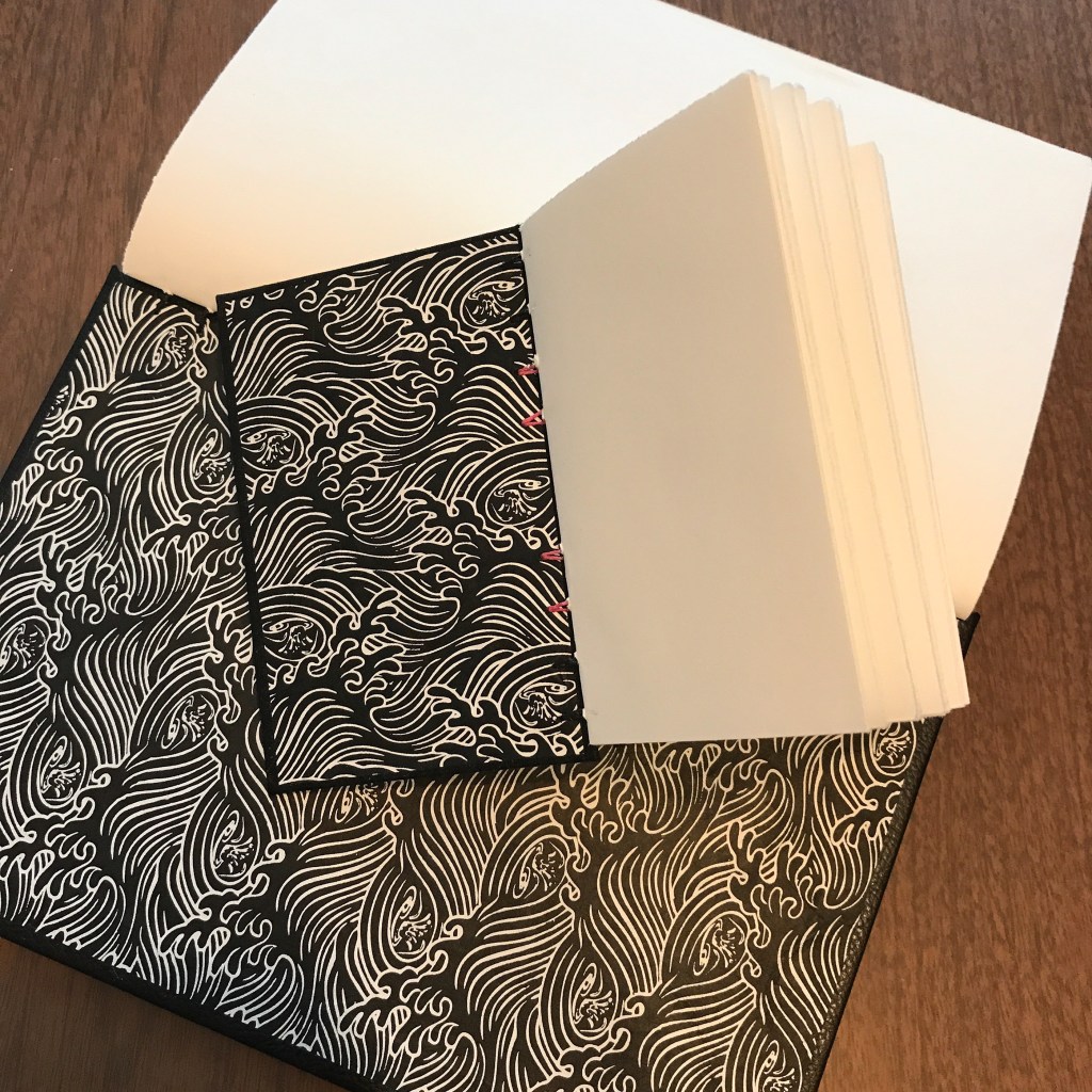 Photo of open small and large journals showing handmade paper with black and white design