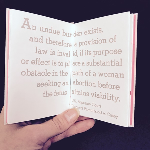 Photo of a page spread held open in a hand - large silver text runs across both pages