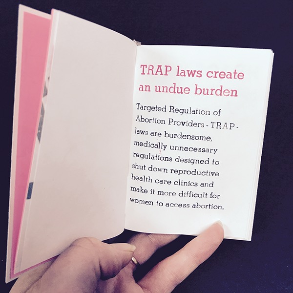 Photo of a page spread held open in a hand - pink and black text visible on the right page