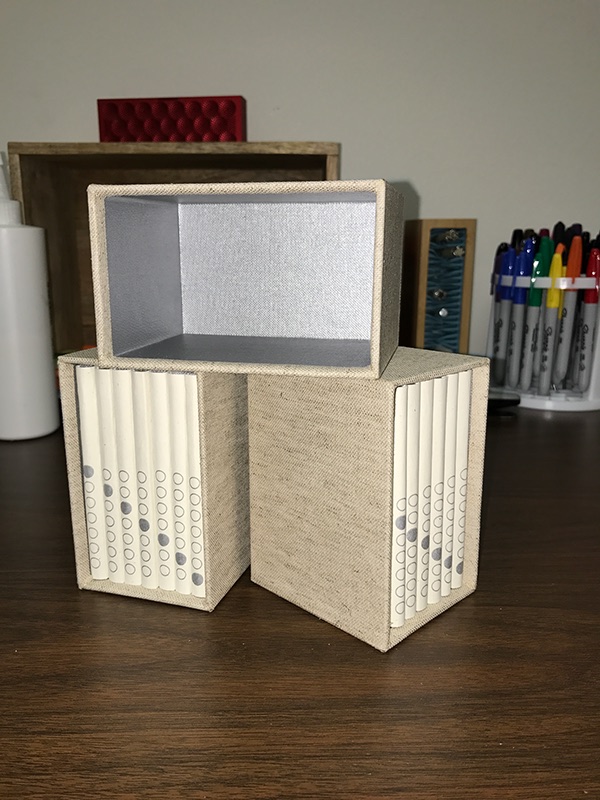 Photo showing two cased sets of books with a third case empty sitting on top and turned sideways to show the silver cloth inside