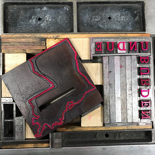 Photo of letterpress bed with Louisiana die cut, "Undue Burden" text and letterpress furniture